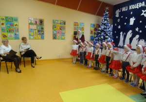 Grupa dzieci wraz z panią dyrektor Marią Królikowska i panią Agnieszką Piekarską śpiewają kolędy.